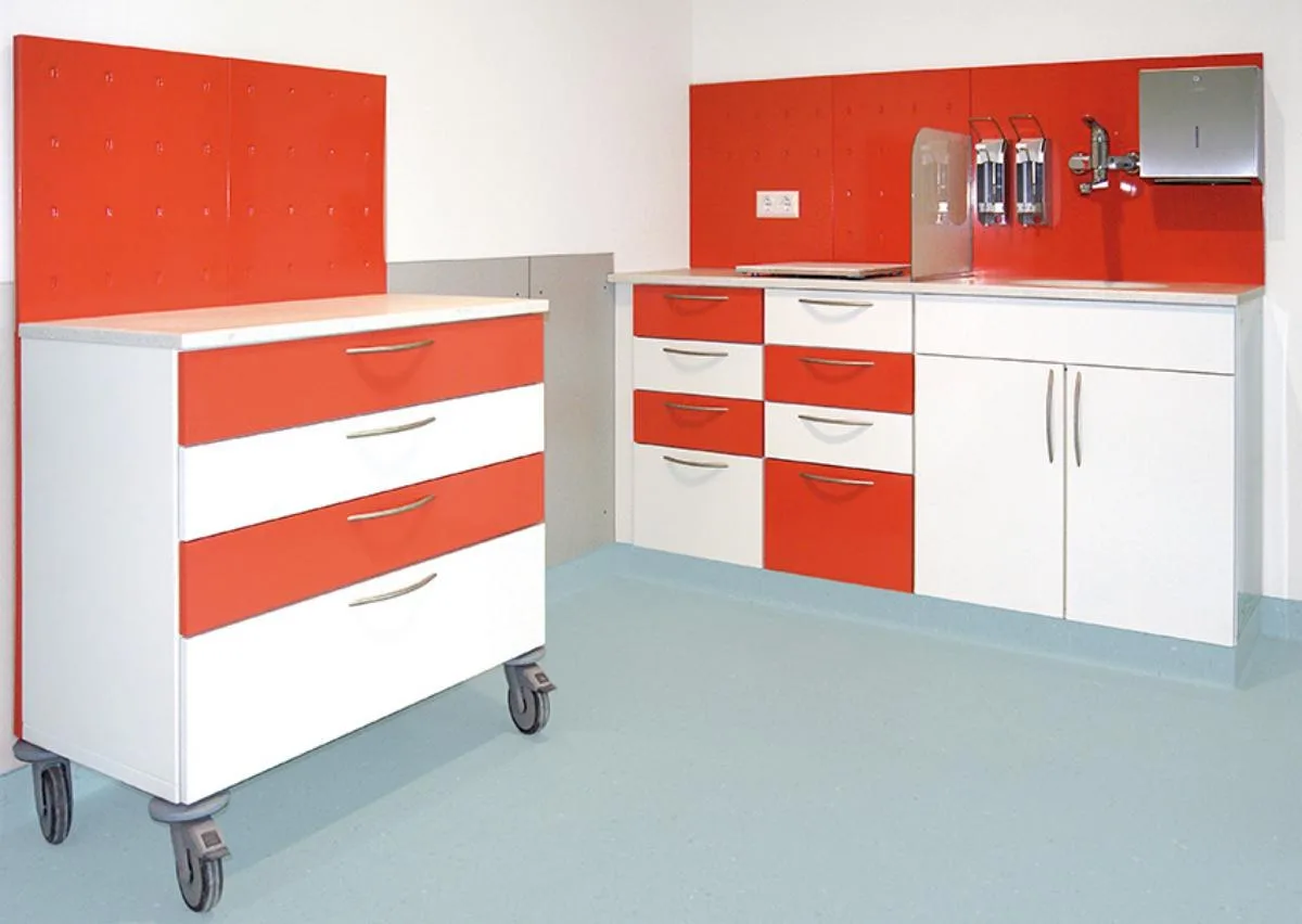 Weiße Möbelzeile mit roten Schubladen und roter Rückwand, davor ein fahrbarer Container