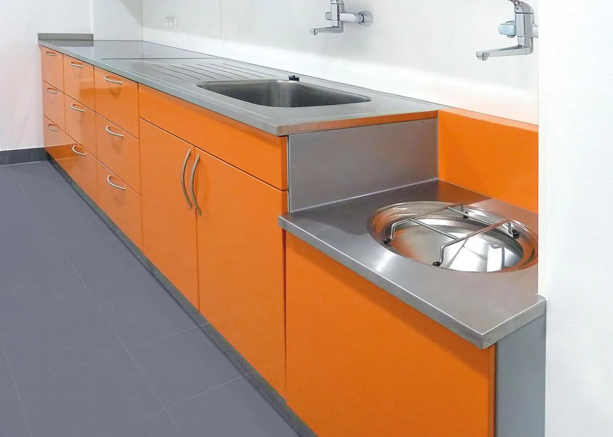 Möbelzeile mit orangen Fronten, Edelstahl-Arbeitsplatte und eingelassenem Edelstahlbecken